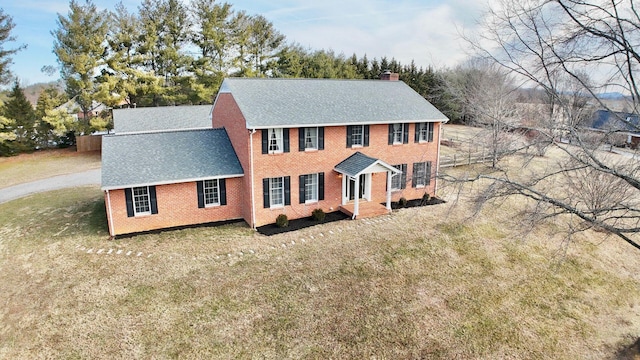 view of front of house featuring roof with shingles, brick siding, a chimney, and a front yard