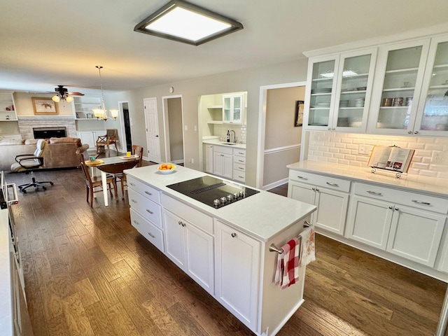 kitchen featuring black electric stovetop, a sink, white cabinetry, light countertops, and glass insert cabinets