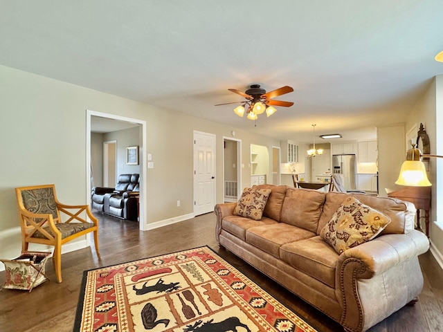 living room with ceiling fan with notable chandelier, dark wood finished floors, and baseboards