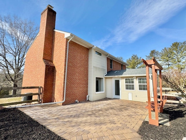 rear view of house with a patio, brick siding, a chimney, and fence