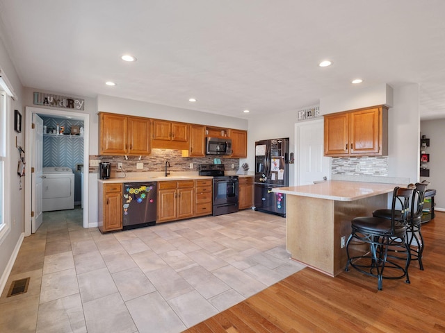 kitchen featuring washer / clothes dryer, light countertops, visible vents, a sink, and black appliances