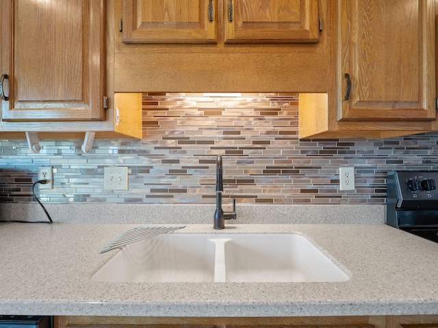 kitchen featuring black range with electric stovetop, light stone counters, a sink, and tasteful backsplash