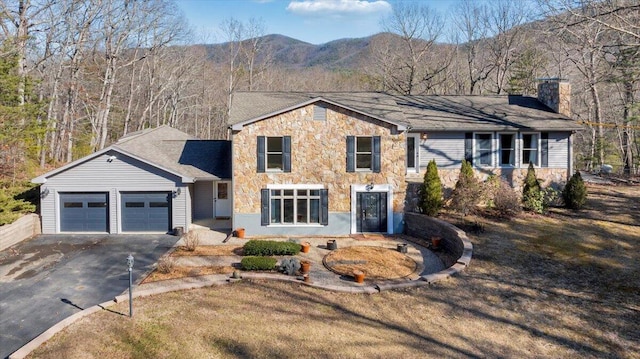 view of front of house with aphalt driveway, a chimney, an attached garage, a mountain view, and stone siding