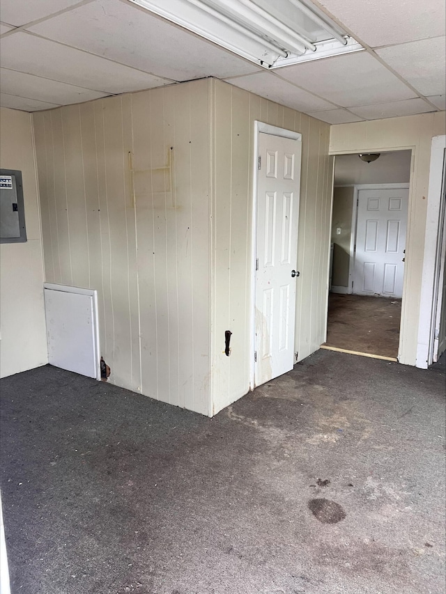 unfurnished room featuring a paneled ceiling, wooden walls, and electric panel