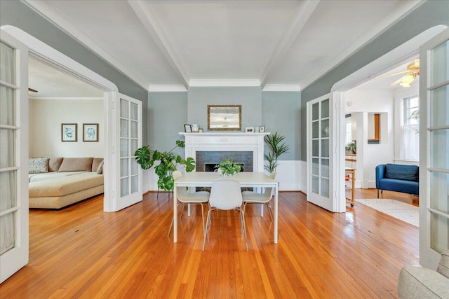 dining area with ornamental molding, french doors, a fireplace, and light wood-style flooring