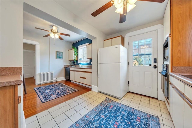 kitchen with black dishwasher, radiator heating unit, freestanding refrigerator, light tile patterned flooring, and stainless steel oven