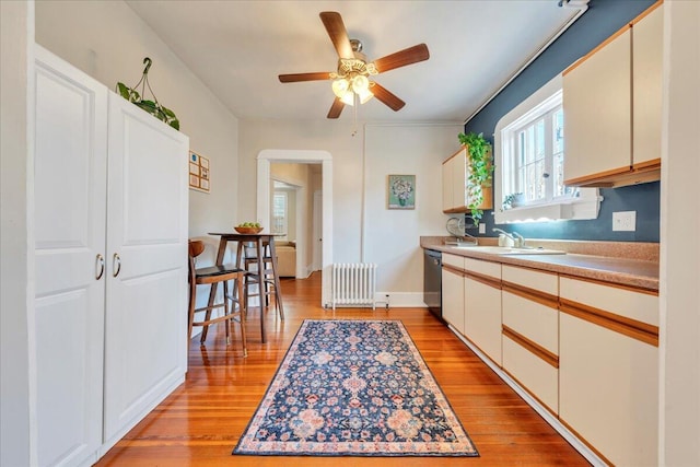 kitchen featuring a sink, light countertops, stainless steel dishwasher, light wood finished floors, and radiator heating unit