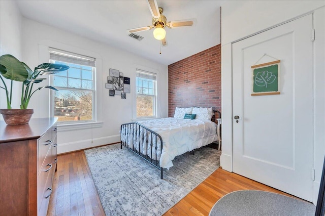 bedroom featuring light wood finished floors, baseboards, visible vents, brick wall, and ceiling fan