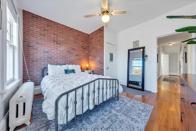 bedroom featuring hardwood / wood-style floors, ceiling fan, brick wall, access to outside, and baseboards