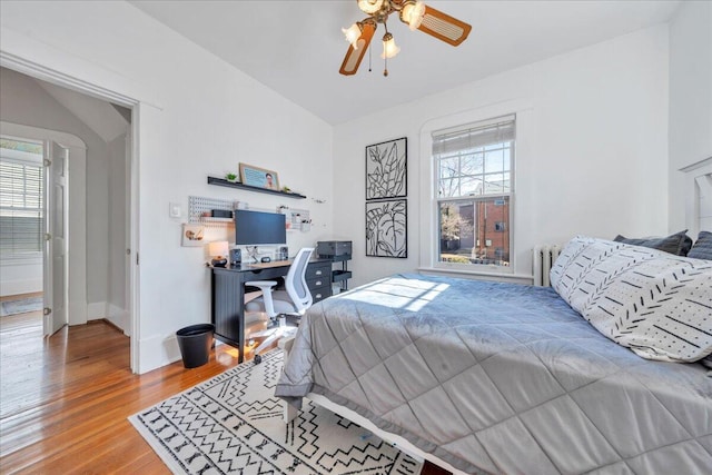 bedroom featuring radiator heating unit, multiple windows, baseboards, and wood finished floors