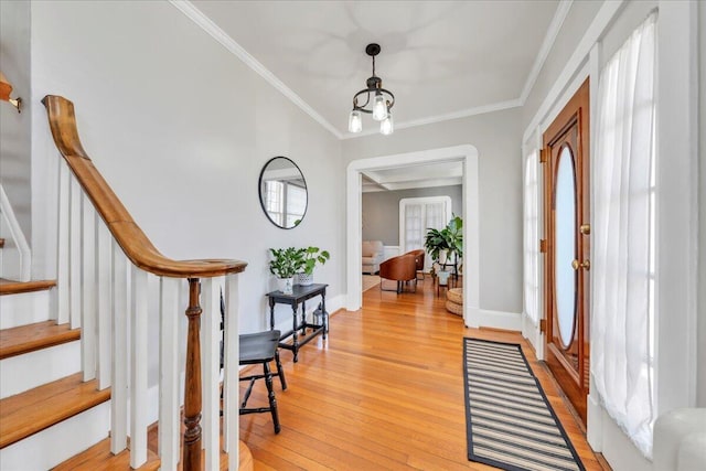 foyer featuring light wood-type flooring, crown molding, baseboards, and stairs