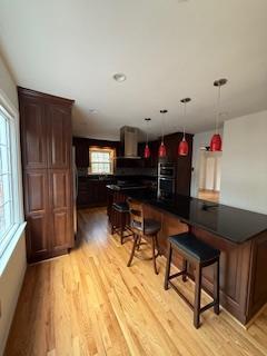 kitchen featuring light wood finished floors, a kitchen breakfast bar, dark countertops, and ventilation hood