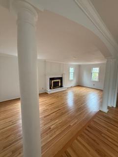 unfurnished living room with crown molding, a glass covered fireplace, wood finished floors, and ornate columns