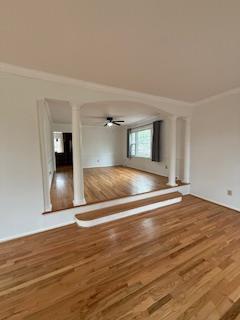 unfurnished living room with wood finished floors, a fireplace with raised hearth, and a ceiling fan