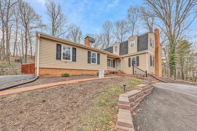 view of front of home with a shingled roof, entry steps, fence, and a chimney