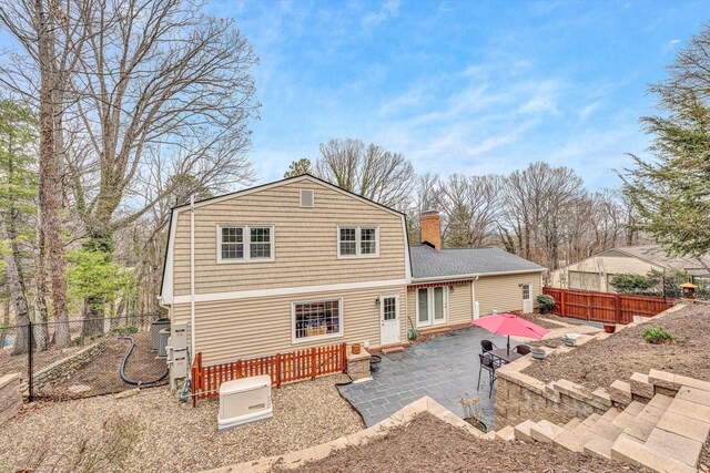 back of property featuring a gambrel roof, a fenced backyard, a chimney, and a patio