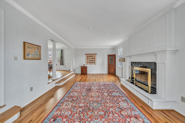 living area with a wealth of natural light, a glass covered fireplace, light wood finished floors, and decorative columns