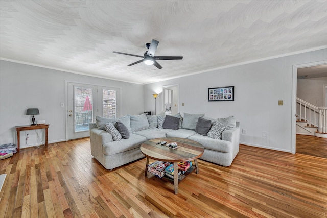 living room featuring stairs, hardwood / wood-style flooring, baseboards, a ceiling fan, and crown molding
