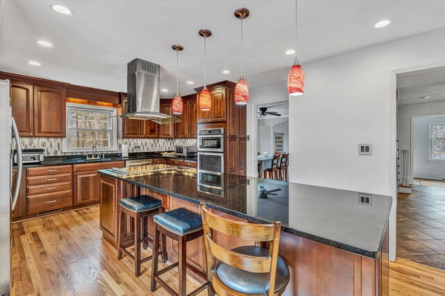 kitchen with a kitchen breakfast bar, island exhaust hood, light wood-type flooring, recessed lighting, and decorative backsplash