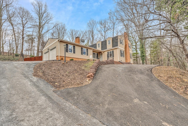 view of front facade featuring a garage, driveway, a chimney, and fence