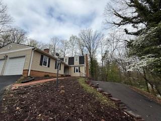 view of home's exterior featuring a chimney, an attached garage, and driveway