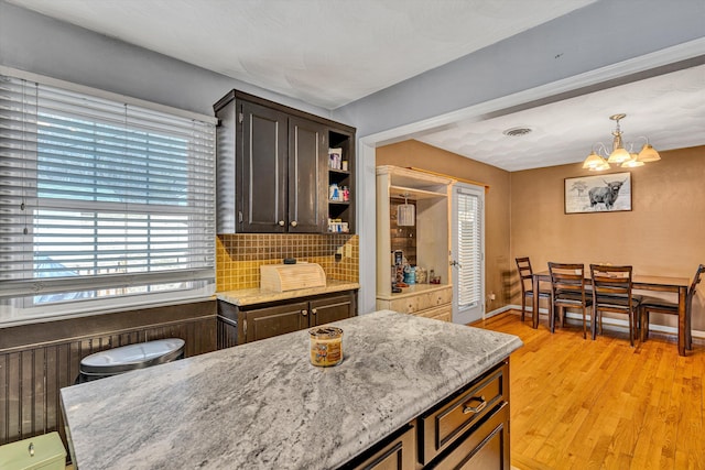 kitchen with pendant lighting, open shelves, tasteful backsplash, light wood-style flooring, and light stone countertops