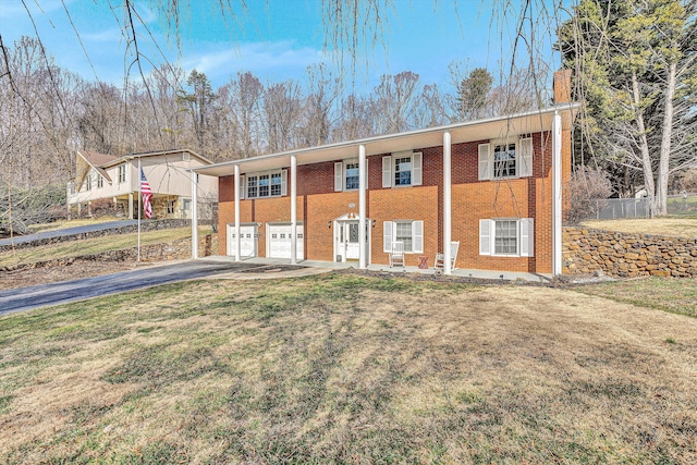 view of front of house with brick siding, an attached garage, a front yard, fence, and driveway