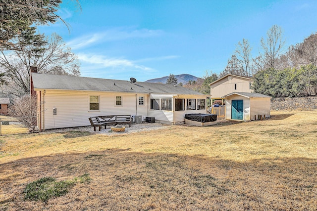 rear view of property featuring an outbuilding, an outdoor fire pit, cooling unit, a storage shed, and a lawn