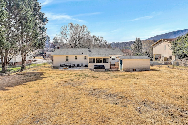 rear view of property featuring a mountain view, a storage shed, an outdoor structure, fence, and a lawn