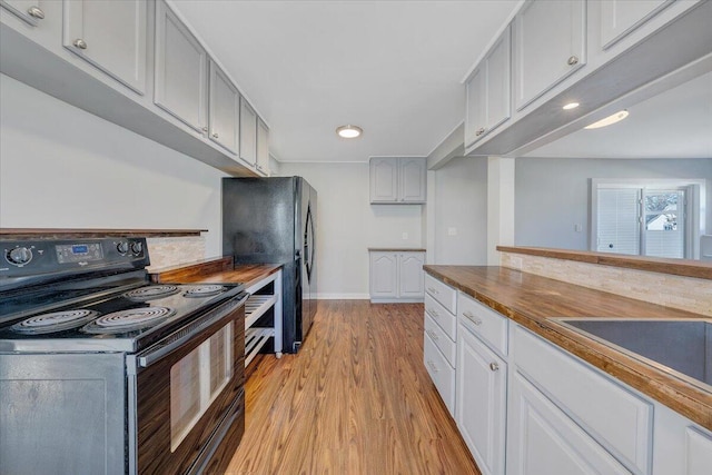 kitchen with light wood-type flooring, black appliances, white cabinetry, wooden counters, and a sink