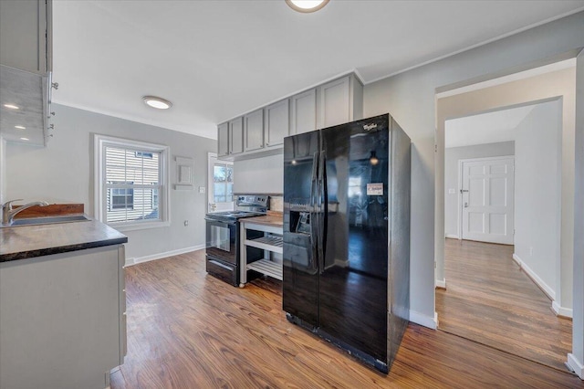 kitchen with electric stove, dark countertops, black fridge with ice dispenser, gray cabinetry, and a sink