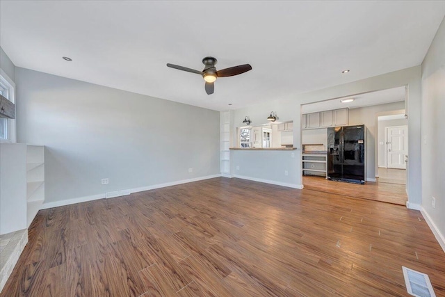 unfurnished living room with visible vents, a ceiling fan, wood finished floors, plenty of natural light, and baseboards