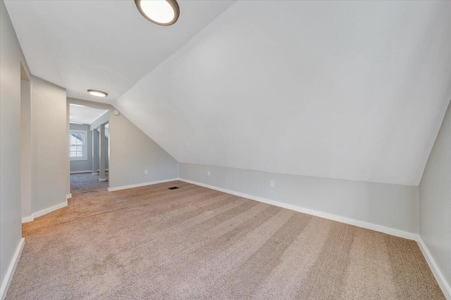 additional living space featuring lofted ceiling, light colored carpet, visible vents, and baseboards