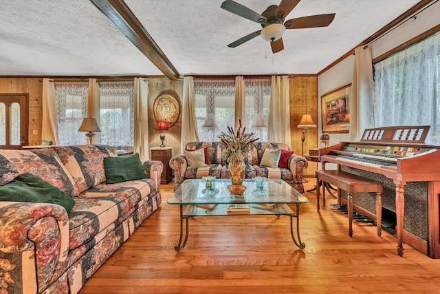 living area featuring a textured ceiling, light wood-style flooring, a ceiling fan, beamed ceiling, and crown molding