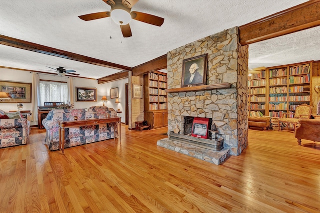 living area with beam ceiling, a stone fireplace, a textured ceiling, and light wood finished floors