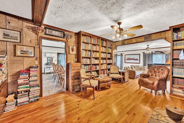 living area with light wood-style floors, ceiling fan, ornamental molding, and a textured ceiling