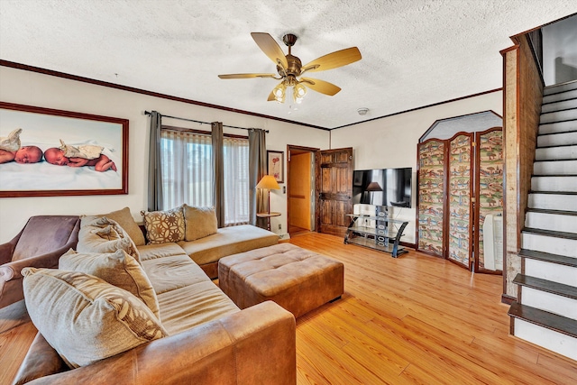 living area featuring ceiling fan, a textured ceiling, stairs, ornamental molding, and light wood finished floors