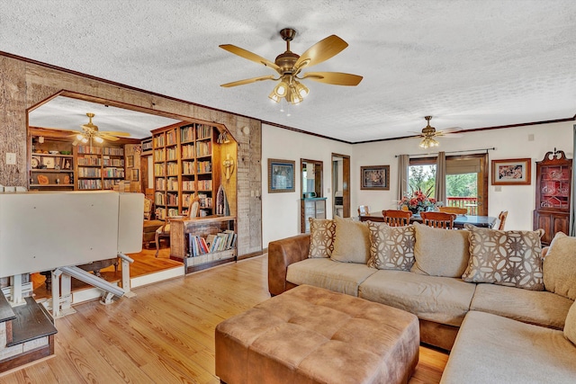 living area with ornamental molding, ceiling fan, light wood-style flooring, and a textured ceiling