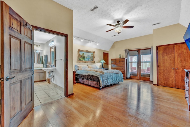 bedroom with vaulted ceiling, light wood finished floors, a textured ceiling, and visible vents