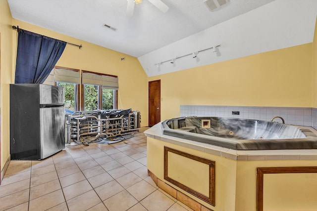 kitchen with tile counters, visible vents, freestanding refrigerator, light tile patterned flooring, and vaulted ceiling