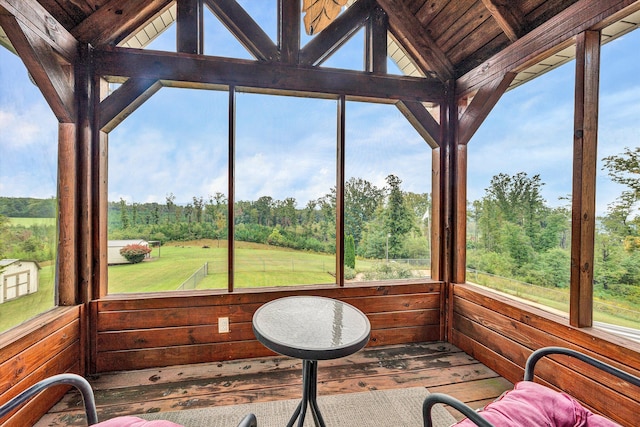 unfurnished sunroom featuring vaulted ceiling, a view of trees, wooden ceiling, and a healthy amount of sunlight