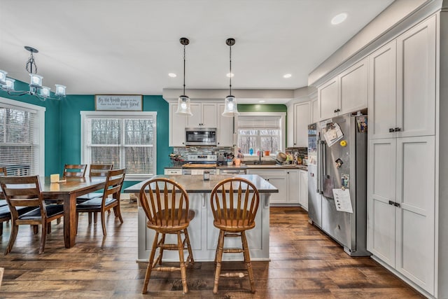 kitchen featuring a kitchen breakfast bar, dark wood-type flooring, a center island, stainless steel appliances, and backsplash