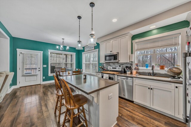 kitchen featuring a kitchen island, appliances with stainless steel finishes, dark wood-style flooring, and a sink