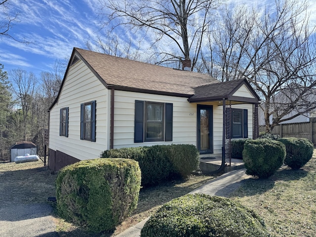 bungalow-style home with roof with shingles, a chimney, and fence