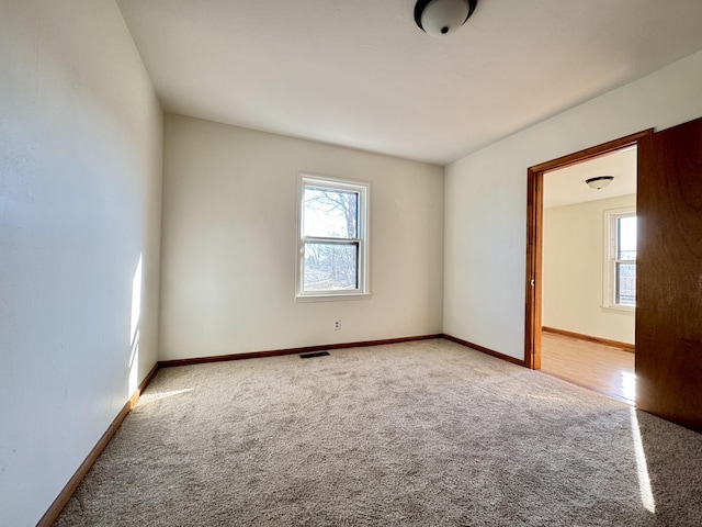 carpeted spare room featuring a wealth of natural light, visible vents, and baseboards