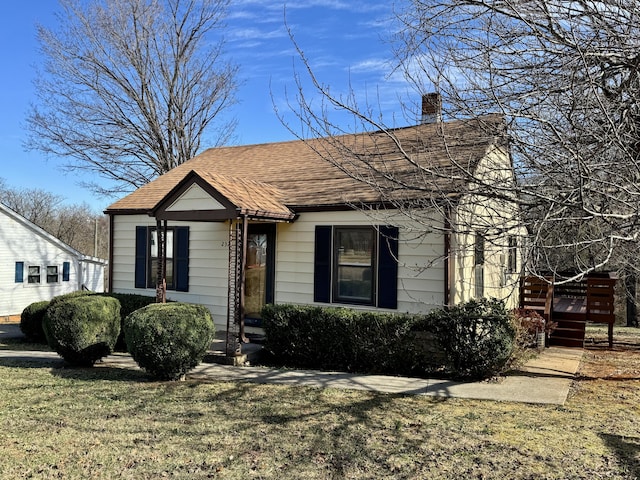 view of front facade featuring a chimney, roof with shingles, and a front yard