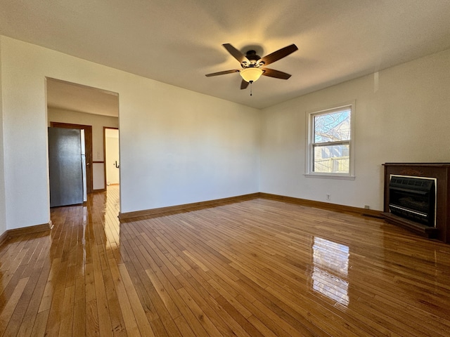 unfurnished living room with ceiling fan, wood-type flooring, a fireplace, and baseboards