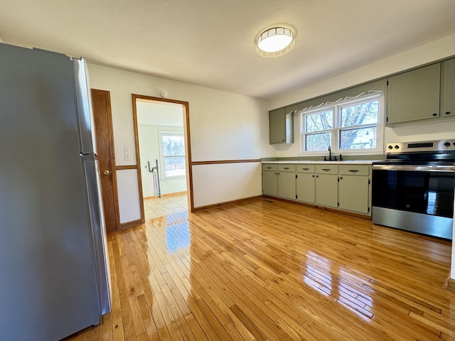 kitchen featuring stainless steel appliances, baseboards, light countertops, and light wood finished floors