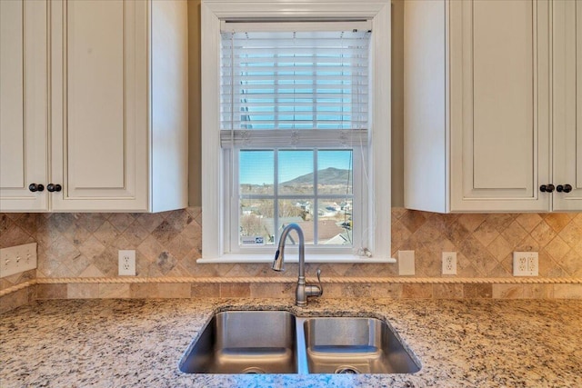 kitchen with tasteful backsplash, white cabinetry, a sink, and light stone countertops