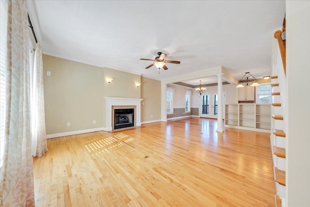 unfurnished living room with a fireplace with flush hearth, baseboards, light wood finished floors, and ceiling fan with notable chandelier